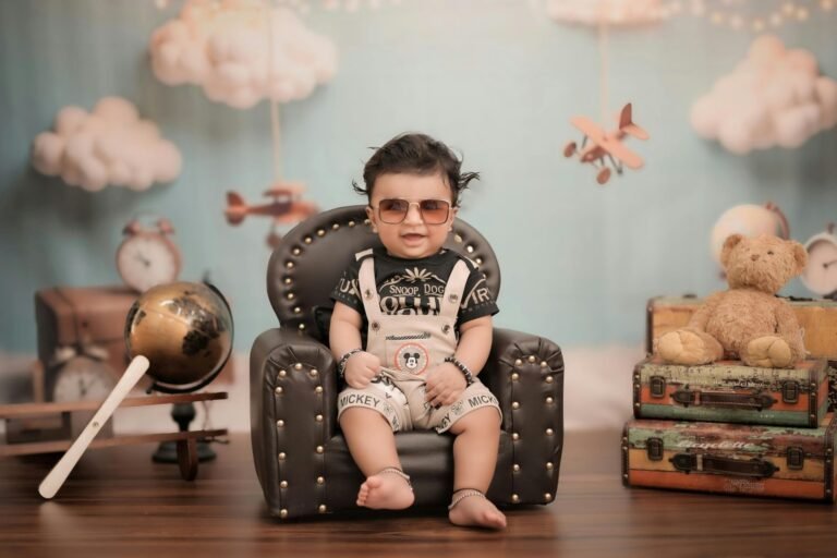 Baby wearing sunglasses sitting in a chair with a travel themed background.