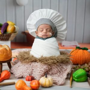 A sleeping baby dressed as a chef surrounded by bread and vegetables