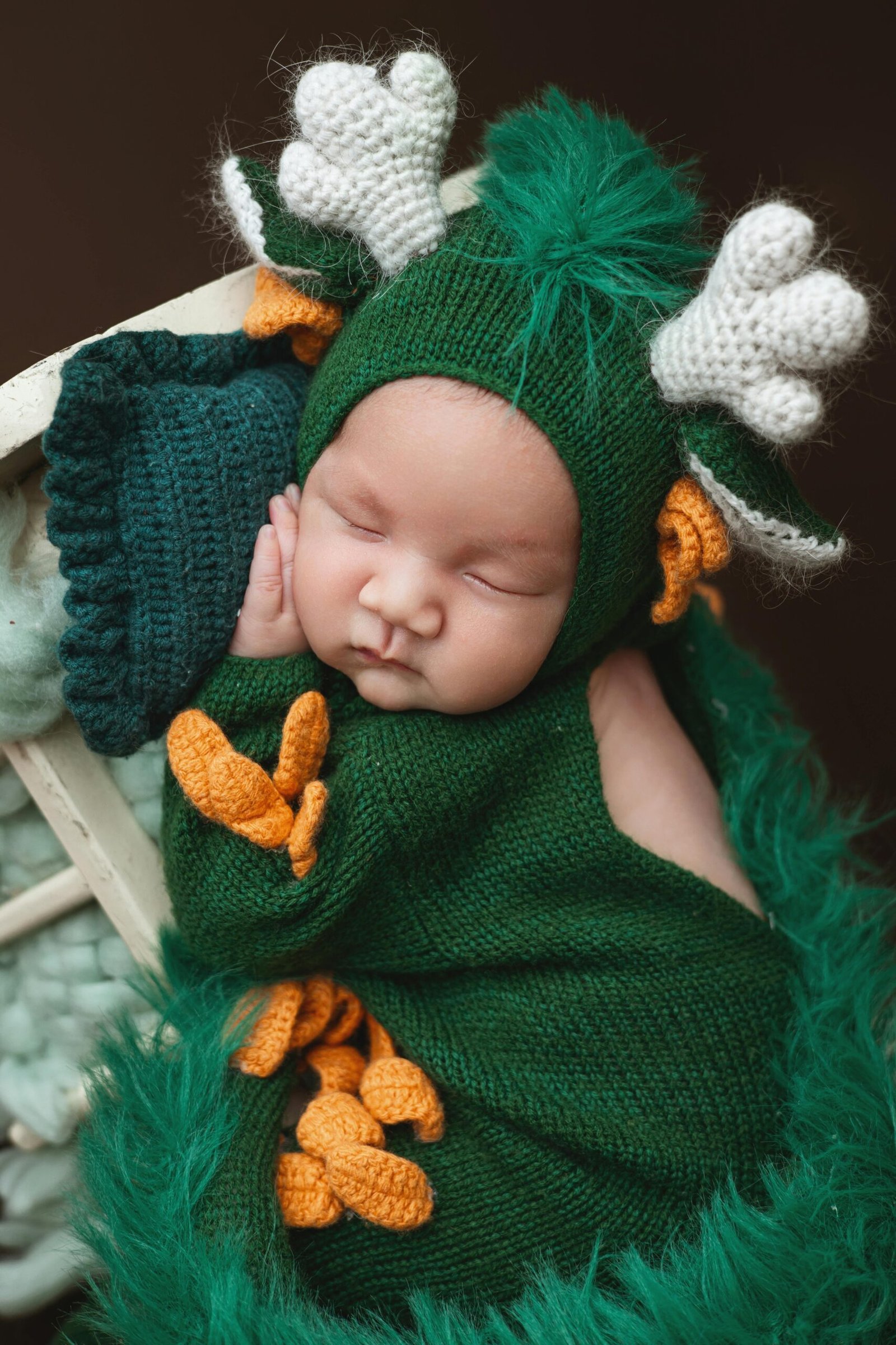 Sleeping baby dressed in a green knitted deer outfit.
