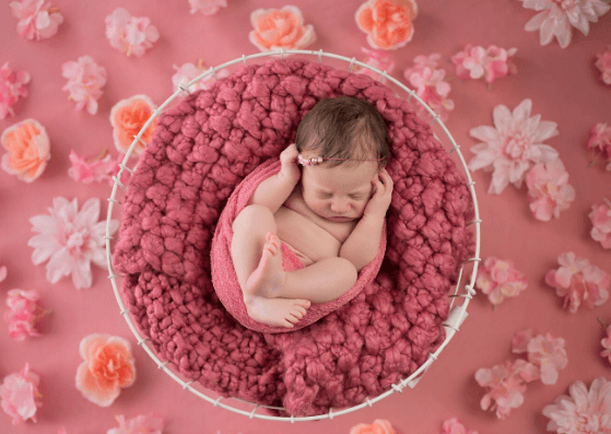 Sleeping newborn wrapped in pink, lying in a basket surrounded by flowers