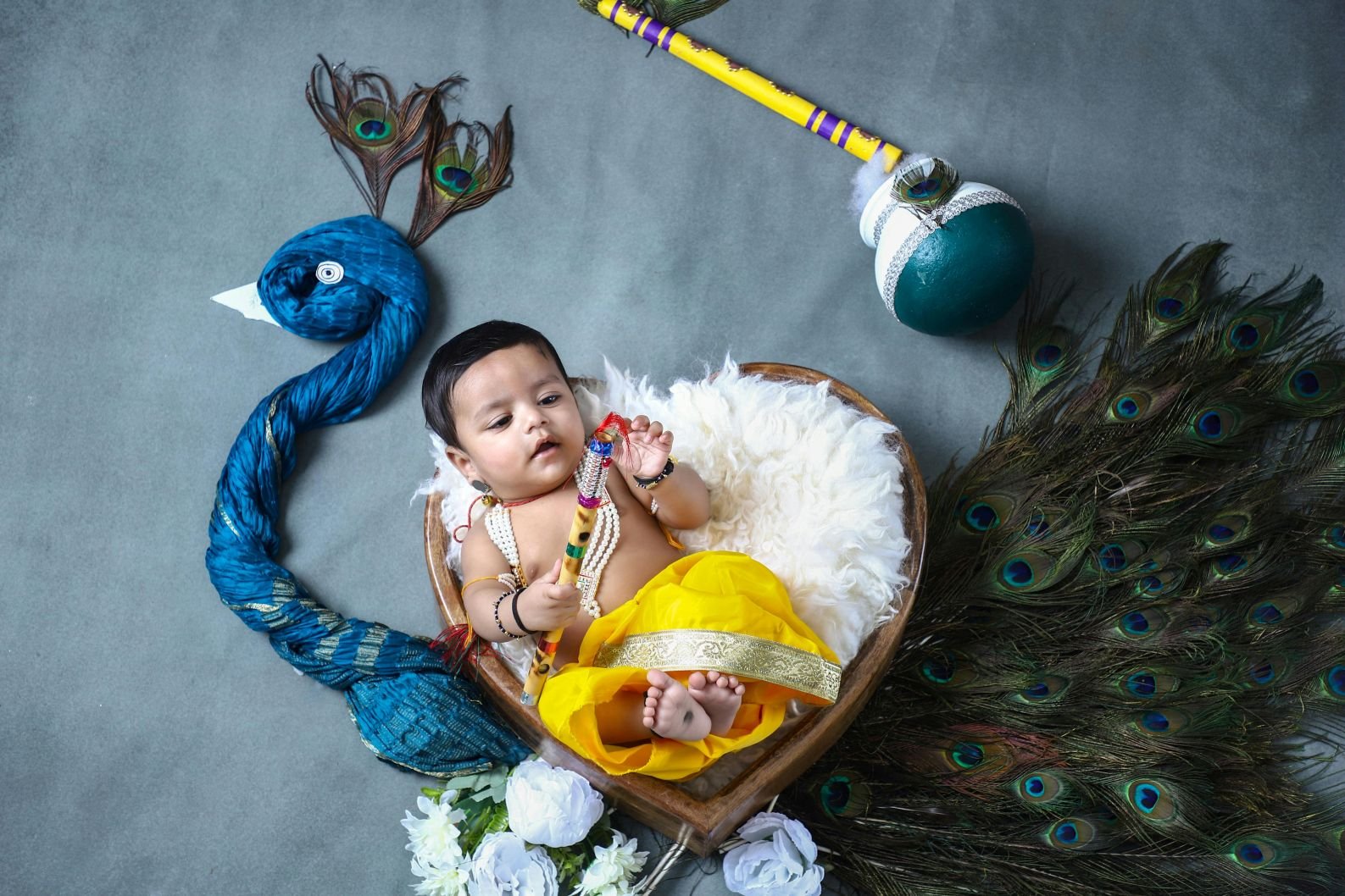 Baby dressed as Krishna in a basket with peacock feathers and a flute.