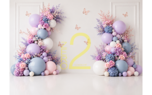Pastel baby girl photography backdrop with lavender, pink and blue balloons, floral arrangements, butterflies and cream paneled wall
