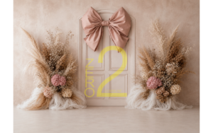 Baby girl photography backdrop with cream paneled door, blush-pink satin bow, and beige floral arrangements