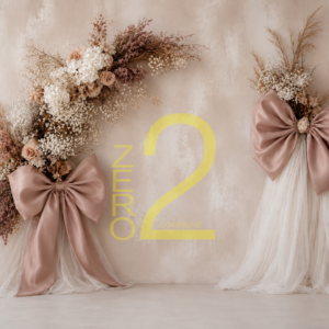 Baby girl photography backdrop with a textured beige wall, white draped fabric, botanical floral arrangements, and oversized dusty pink bows.