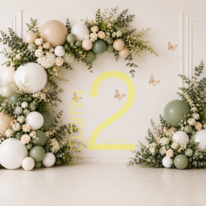 Sage green and white floral baby girl birthday backdrop with pastel balloons, botanical greenery, blush flowers, butterflies, and white wall panelling.