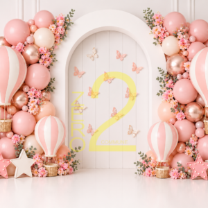 Pink hot air balloon baby girl birthday backdrop with pastel balloon clusters, butterflies, floral decorations, and a white arched panel.
