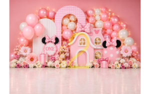 Pink mouse theme first birthday photography backdrop with pink balloon arch, decorative houses, bows and flowers